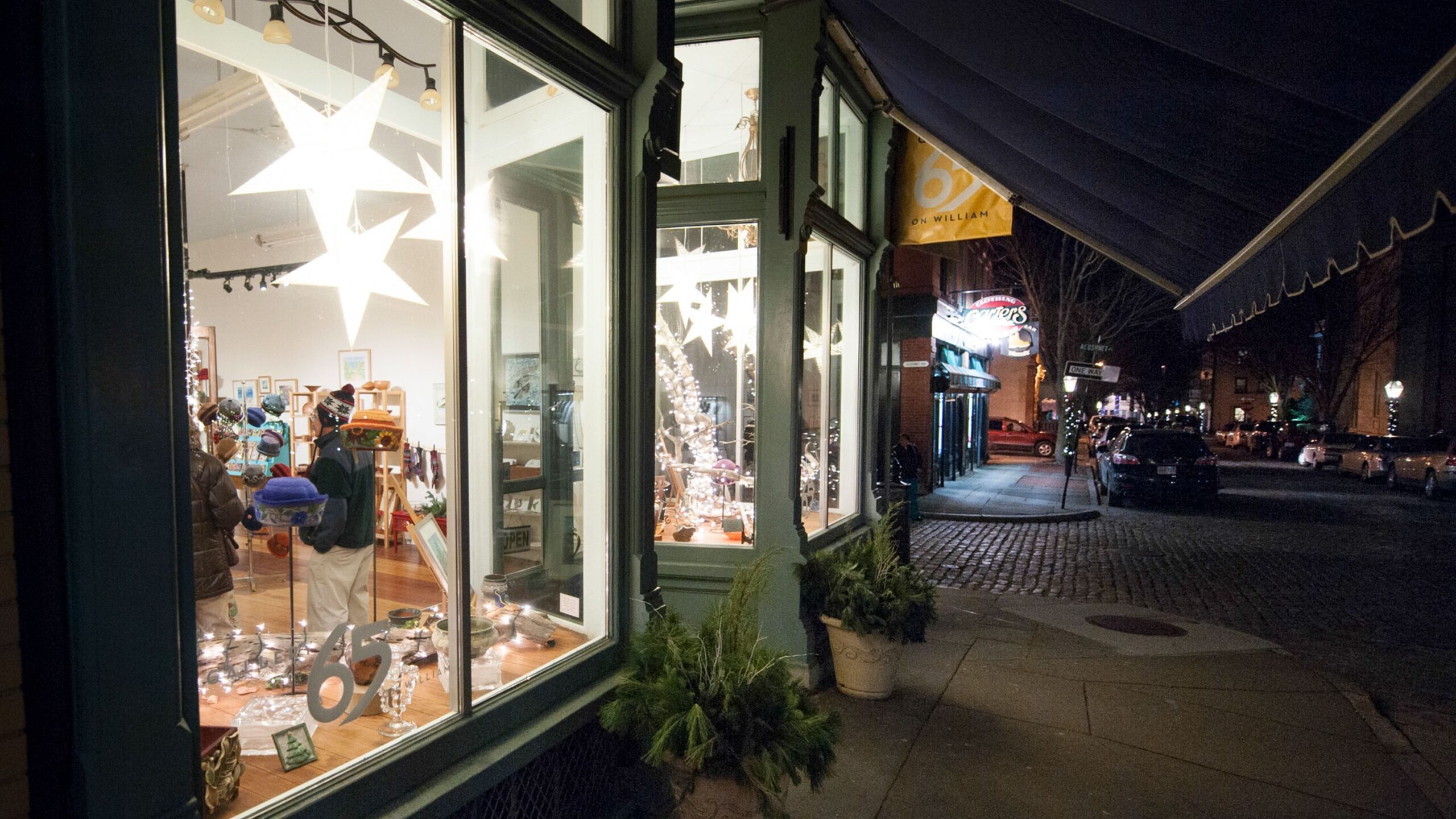 The brightly-lit window of a shop decorated for the holidays illuminates the street outside.