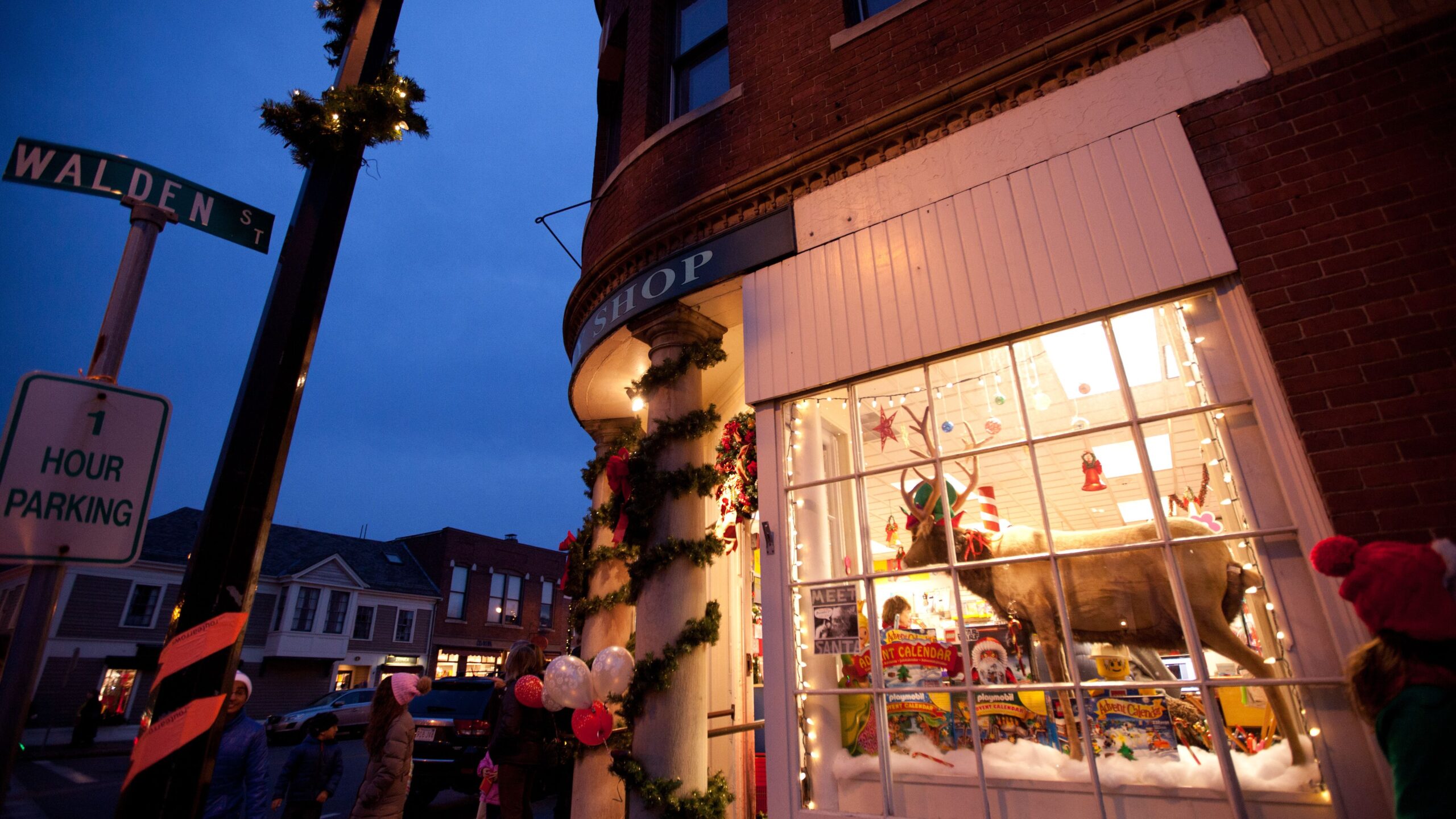 A stuffed reindeer sits inside a brightly-lit shop window decorated for the winter holidays.