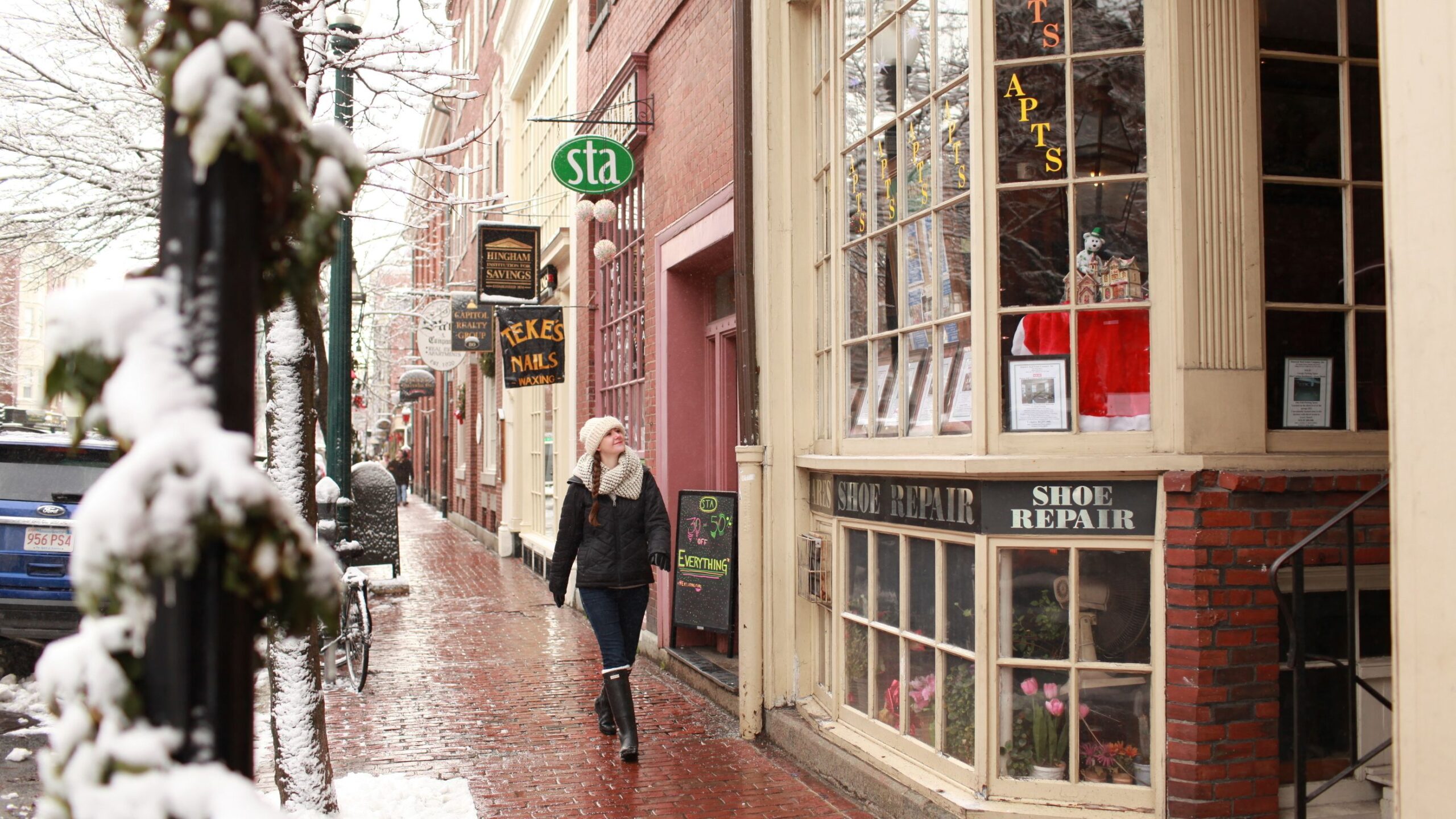 A woman walks along a Boston street outside, admiring shop windows and freshly-fallen snow along the way.